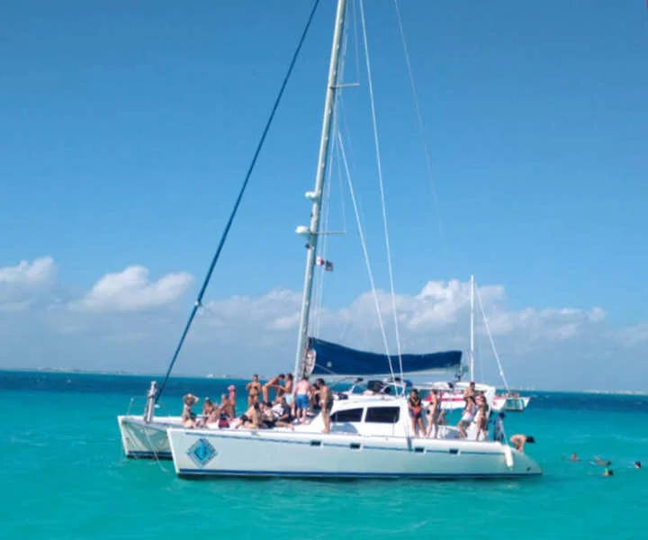 Personas disfrutando un paseo abordo de un catamarán rumbo a Isla Mujeres, preparándose para practicar snorkel en los arrecifes